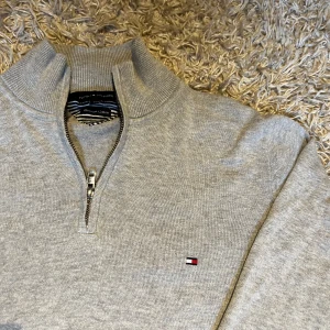 Grå half zip tröja Tommy Hilfiger - Snygg ljusgrå tröja från Tommy Hilfiger i bomull med halv dragkedja och liten broderad logga på bröstet. Ribbstickad krage, ärmslut och nederkant ger en clean look. Postas antigen samma dag som köp eller dagen därpå🙌💯