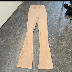 Beiga bootcut byxor från 157 XS - Snygga beiga bootcut-byxor från 157 i mjukt stretchigt material. De har hög midja och en figurnära passform upptill som går ut i vida ben. Perfekta för dig som gillar en clean och trendig look.