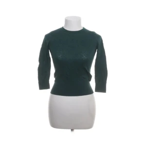 Mörkgrön stickad tröja med trekvartsärm - Mörkgrön stickad tröja med rund halsringning och trekvartsärmar. Tröjan har en åtsittande passform med bred ribbad mudd i midjan och vid ärmsluten. Perfekt för dig som gillar en enkel men stilren look.