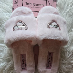 Juicy Couture fluffiga rosa tofflor 40 - Supermjuka och fluffiga sandaler från Juicy Couture i ljusrosa syntetmaterial. Överdelen pryds av ett hjärta med rosa stenar och silverfärgad Juicy-logga. Sula i ljusrosa med räfflad undersida för extra grepp. Perfekta för en glam touch hemma.