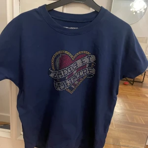 Mörkblå t-shirt med hjärtmotiv - Snygg mörkblå t-shirt från Zadig & Voltaire med ett stort hjärtmotiv i glittriga stenar på bröstet. Klassisk rund halsringning och korta ärmar. Perfekt statement-plagg för dig som gillar coola detaljer och vill sticka ut.