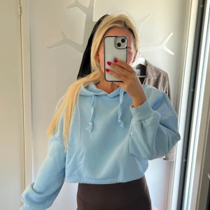 Ljusblå croppad hoodie med huva - Säljer en ljusblå croppad hoodie med huva och snörning. Tröjan har oversized passform, långa ärmar med breda muddar och är tillverkad i mjuk bomullsmix. Perfekt för en chill och avslappnad stil.