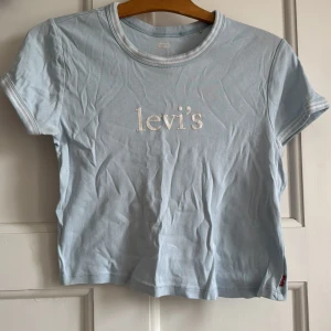 Ljusblå Levi's t-shirt med logga - Snygg ljusblå t-shirt från Levi's med vit broderad logga framtill. Klassisk passform med korta ärmar och rund hals. Tillverkad i mjuk bomull, perfekt för en chill och stilren look. Diskreta vita detaljer på ärmslut och halsringning.
