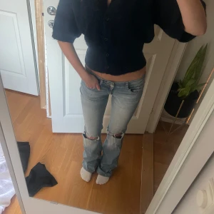 Ljusblå bootcut jeans med hål vid knäna - Säljer ett par ljusblå jeans med bootcut passform och slitna hål vid båda knäna. Jeansen har låg midja, klassiska fickor fram och bak med knappdetaljer på bakfickorna. (Jag är 167 cm lång och har innerbenslängd 80) Hör av dig om du undrar över något!💕
