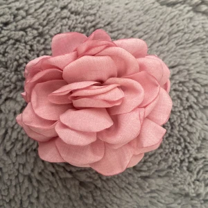 Rosa blommigt diadem med tygblomma - Superfint diadem med stor rosa tygblomma som ger en romantisk och söt look. Blomman är gjord av mjukt tyg och sitter på ett genomskinligt hårspänne, perfekt för att piffa upp frisyren. Passar perfekt till vår och sommar för en extra touch.