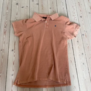 Orange pikétröja från Morris, storlek L - Snygg orange pikétröja från Morris i storlek L. Klassisk krage, korta ärmar och broderad logga på bröstet. Tillverkad i bomull för en skön känsla. Perfekt för en avslappnad och stilren look.