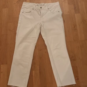 Vita raka jeans  - Snygga vita denim jeans med raka ben och råa, fransiga benslut. Klassisk femficksmodell med bälteshällor och silverfärgade nitar. Perfekta för dig som vill ha en clean och fräsch look med en twist.
