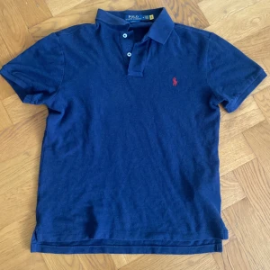 Marinblå pikétröja Polo Ralph Lauren - Marinblå pikétröja från Polo Ralph Lauren i slim fit-modell. Klassisk krage, korta ärmar och knäppning med två knappar. Fick i julklapp förra året vet ej nypris. Skriv vid funderingar😁