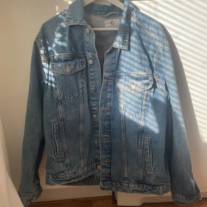 Blå jeansjacka från C Scandinavian Design - Säljer en klassisk blå jeansjacka från C Scandinavian Design i storlek XL. Jackan har två bröstfickor med knappar, två sidofickor och knappar framtill. Perfekt för dig som gillar en tidlös och avslappnad stil.