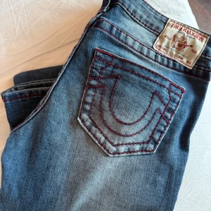 True Religion Ultra Low Rise Flare Jeans - Snygga blå bootcut jeans från True Religion med klassisk logga på bakfickan och markerade sömmar. Jeansen har låg midja och är tillverkade i jeansmaterial med lätt tvättad look. Dessa är använda två gånger och är som ny! 