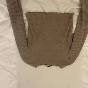 Beige ribbad långärmad tröja - Säljer en beige ribbad långärmad tröja med tight passform. Tröjan har en enkel och stilren design med raka linjer och stretchigt material som sitter snyggt på kroppen. Perfekt att matcha med jeans eller kjol för en clean look.