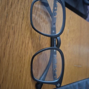 Chrome hearts inspirerade glasögon - Snygga svarta glasögon med fyrkantiga bågar och coola silverdetaljer. Ramen är i matt svart plast och ger en modern vibe. Perfekta för dig som vill sticka ut med en trendig accessoar.