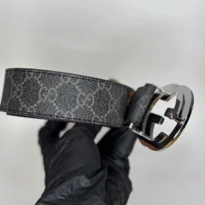 Svart GG-bälte  - Snyggt svart bälte med klassiskt GG-mönster och stor silverfärgad GG-spänne. Bältet är gjort i skinn och har en lyxig känsla med detaljer i grått. Perfekt accessoar för att lyfta vilken outfit som helst.