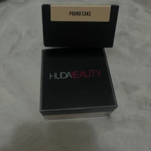 Huda Beauty Easy Bake Pound Cake puder - Loose baking & setting powder från Huda Beauty i nyansen Pound Cake. Kommer i en snygg svart förpackning med transparent botten och rosa/vit logga. Perfekt för att fixera sminket och ge en matt finish.