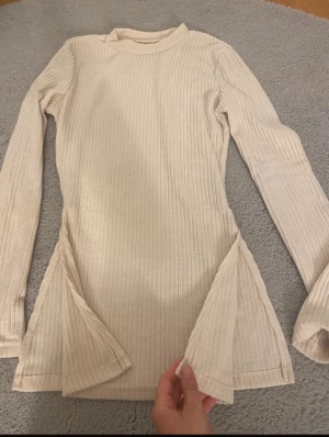 Beige ribbad långärmad topp - Säljer en beige ribbad långärmad topp med slitsar på båda sidorna nedtill. Toppen har en enkel, rund hals och är figurnära i modellen. Materialet är mjukt och stretchigt, perfekt för en chill och stilren look. Från SHEIN 