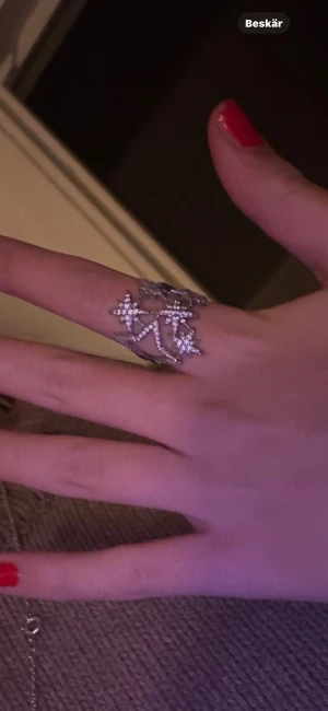 Silvrig ring med stjärndetaljer - Säljer en cool och unik silvrig ring med flera små stjärnor som sitter ihop i ett öppet mönster. Ringen har en glittrig finish som gör den extra iögonfallande och passar perfekt om du gillar statement-smycken med lite edge.