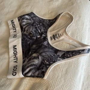 Blå  mönstrade leggings från Mighty Solo plus tillhörande BH-topp - Snygga blåa  leggings från Mighty Solo med tropiskt mönster i grå toner och bred vit resår med logga. Tillverkade i stretchigt material med 73% polyester och 27% spandex, perfekt för träning eller chill. Superskön passform och cool design.Plus BH-topp.Storkek ca xs.Nyskick.