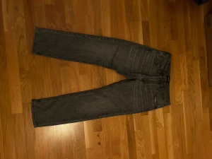 Grå jack&jones jeans med rak passform - Snygga grå jeans med klassisk femficksdesign och rak passform. Jeansen har subtila slitningar och en mörkgrå ton som ger en cool vibe. Tillverkade i jeansmaterial med knapp och knappar framtill. Perfekta för dig som gillar stilrena och tidlösa byxor. Storlek 30 30