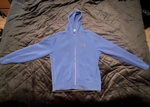 Polo Ralph Lauren Hoodie - Snygg blå hoodie från Polo Ralph Lauren med dragkedja och huva. Tröjan har långa ärmar, två fickor fram och en liten röd logga broderad på bröstet. Storleken är L.