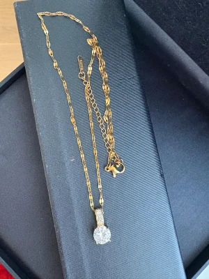 Guldigt halsband med glittrig sten - Snyggt halsband i guldtonad rostfri stål från S.STEEL med en glittrig rund sten som hängsmycke. Kedjan har ett unikt mönster och låset är i klassisk karbinmodell. Perfekt för dig som gillar bling och vill sticka ut med en elegant detalj.