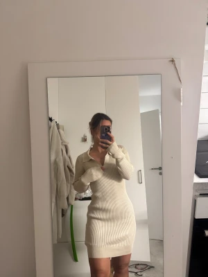 Beige ribbad stickad klänning - Säljer en beige ribbad stickad klänning med krage och v-ringning. Klänningen är kort och har lång ärm, sitter figurnära och är supermjuk. Perfekt för dig som gillar en enkel men snygg look. Jag är xs men passar mig så passar även en xs, S