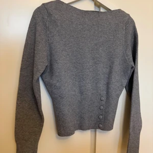 Grå stickad tröja från BikBok  - Vit stickad tröja från Bik Bok med lång ärm och snygga knappar i sidan. Tröjan sitter löst på övre delen och tightare runt midjan, väldigt snygg!! Tröjan är helt ny med prislapp kvar då jag ångrade mig efter köp 🩷