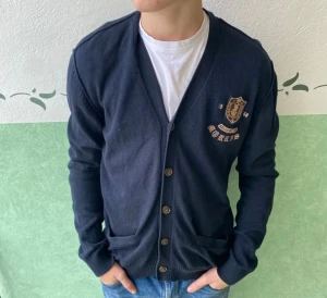 Mörkblå kofta från Morris - Snygg mörkblå kofta från Morris med broderad logga och emblem på bröstet. Koftan har v-ringad hals, knappar framtill och två fickor. Tillverkad i mjuk bomull, perfekt för lager-på-lager och chill stil. Passar dig som gillar klassisk men cool look.