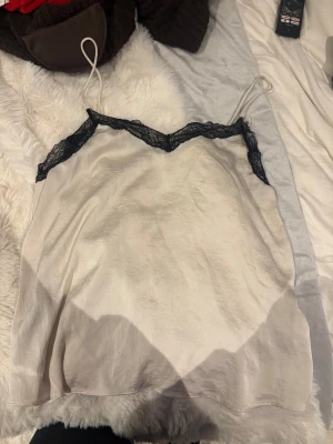 Vit linnetopp med spets från MNG - Vit linnetopp från MNG med tunna axelband och svart spetsdetalj längs v-ringad halsringning. Materialet har en silkeslen finish som ger en lyxig känsla. 