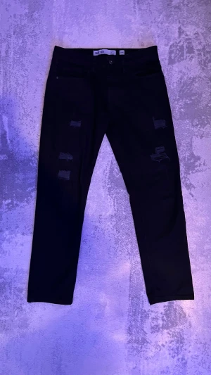 Svarta straight fit jeans med slitningar - Säljer ett par svarta straight jeans från Incode i storlek (31-30)med snygga slitningar på låren och knäna. Jeansen har klassisk femficksmodell och rak passform. Perfekta för dig som gillar en edgy och trendig stil.