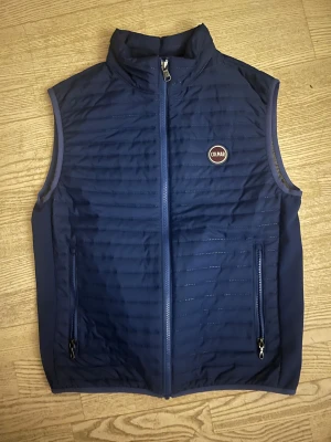 Mörkblå dunväst från Colmar - Snygg mörkblå dunväst från Colmar med quiltad design och två praktiska fickor med dragkedja. Västen har ett stilrent Colmar-märke på bröstet och insidan är grå. Perfekt för lager-på-lager och har en modern, normal passform. Storleken är about XS/S. Använd bara en gång alltså splitterny👍