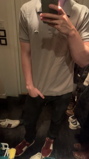 Grå pikétröja från Lacoste - Snygg grå pikétröja från Lacoste med klassisk krage och två knappar framtill. Inga hål i tröjan. Det är bara att höra av sig vid några funderingar.