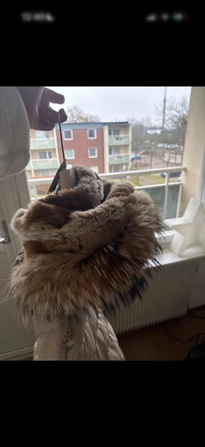 Beige Parajumpers Long Bear dunjacka - Säljer en beige Parajumpers Long Bear dunjacka med fluffig päls på huvan och snygga detaljer som gul rem och broderad patch på ärmen. Jackan har dragkedja, knappar och flera fickor. Perfekt för dig som vill ha en varm och stilren vinterjacka. Den har lite missfärgningar från byxor på insidan men inget man stör sig på eller märker