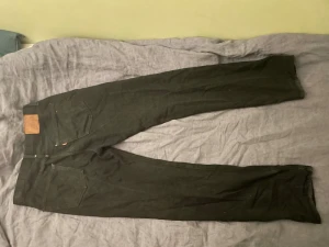 Svarta Levi's 511 jeans straight fit - Svarta jeans från Levi's modell 501 med klassisk femficksdesign och raka ben. Jeansen har en brun läderpatch bak i midjan och guldfärgade nitar framtill. Materialet är slitstarkt denim och passformen är straight med normal midja.