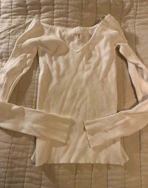 Ribbad vit långärmad topp H&M - Säljer en ribbad vit långärmad topp från H&M med v-ringad hals. Toppen är slim fit och har en mjuk, stretchig känsla som sitter snyggt på kroppen. Perfekt att styla med jeans eller kjol för en clean look.