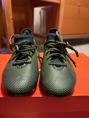 Adidas svarta och gula fotbollsskor - Säljer ett par Adidas fotbollsskor i svart med gula prickar och Adidas-logga på sidan. Skorna har snörning och är tillverkade i syntetmaterial med låg profil och rund tå. Perfekta för dig som vill sticka ut på planen med en cool design.