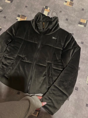 Svart pufferjacka från Reebok XS - Säljer min svarta pufferjacka från Reebok i storlek XS. Jackan har hög krage, dragkedja framtill och diskret Reebok-logga på bröstet. 