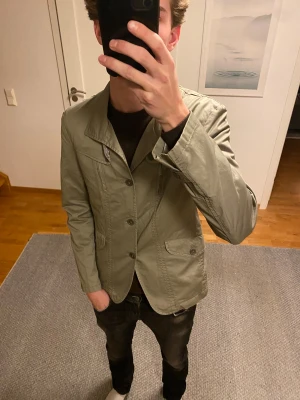 Olivgrön overshirt - Säljer en fet olivgrön kostym overshirt i nytt skick. Hittar inte någon lapp men skulle säga att den passar någon som har S-M. Vet ej märket på den. Skriv för fler frågor.
