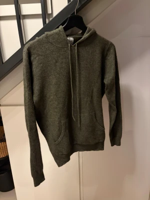Mörkgrön stickad hoodie med huva - Mysig mörkgrön hoodie från John Henric i kashmir. Tröjan har huva med snörning, en stor magficka och långa ärmar. Perfekt för dig som gillar chill och enkel stil. 