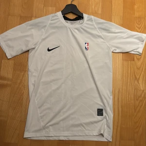 Vit NBA x Nike t-shirt compression - Snygg vit compression shirt från Nike med NBA-logga på bröstet och klassisk svart Nike logga. 