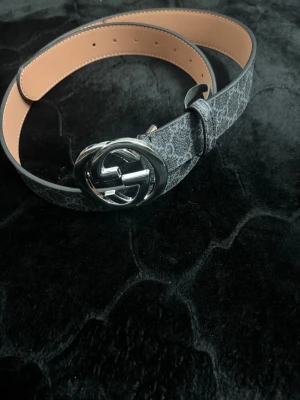 G bälte  - Snyggt svart bälte för ett bra pris. Bältet har ett diskret mönster med Guccis logga över hela bandet och är tillverkat i skinn med en lyxig känsla. Perfekt för att lyfta din outfit med en ikonisk detalj.