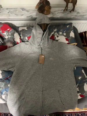 Grå och svart hoodie från Burberry - Två hoodies från Burberry, en i ljusgrått och en i svart. Båda har dragkedja framtill, huva med snörning och stora fickor. Insidan av huvan har ett klassiskt Burberry-mönster. Perfekt för dig som gillar stilrena och bekväma plagg med exklusiv känsla. 500kr styck 