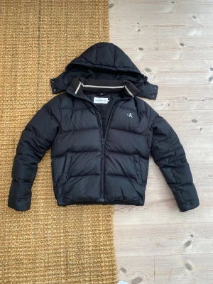 Svart vinterjacka Calvin Klein  - Svart pufferjacka från Calvin Klein Jeans med avtagbar huva och dragkedja framtill. Väldigt bra skick, storlek s.  Mitt pris 689kr kom dm vid funderingar 😁