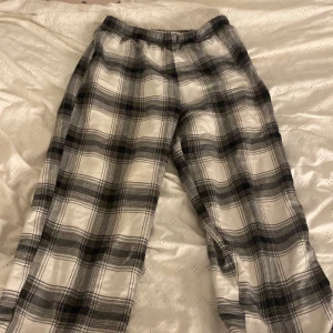 Rutig mjukisbyxa från H&M - Säljer ett par sköna mjukisbyxor från H&M i storlek 146/152. Byxorna har ett svartvitt rutigt mönster och är tillverkade i mjukt bomullsmaterial. De har elastisk midja för extra komfort och passar perfekt för chill dagar hemma.