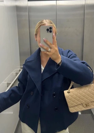 Mörkblå skepparkavaj med bred krage - Säljer en stilren mörkblå skepparkavaj med bred krage och dubbelknäppning framtill. Jackan har en loose passform och är tillverkad i ullmaterial som ger en lyxig och varm känsla. Perfekt för dig som gillar klassisk och cool stil.