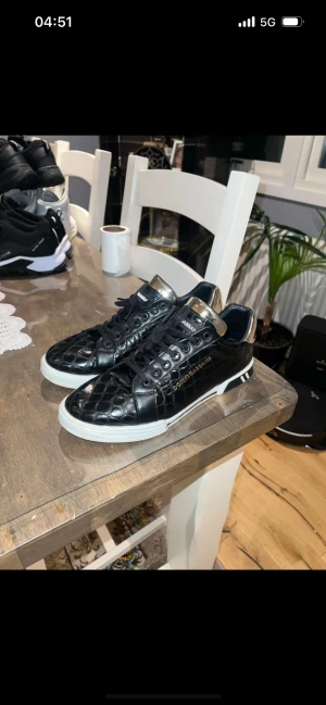 Svarta sneakers från Dolce & Gabbana - Säljer ett par svarta sneakers från Dolce & Gabbana med coolt krokodilpräglat mönster och metallic-detaljer i guld på hälen. Skorna har snörning, vit platt sula och D&G-logga på baksidan. Insidan har en färgglad etikett med varumärket. Riktigt snygga och unika skor!