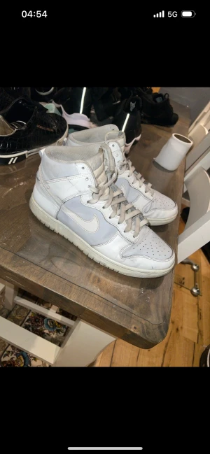 Nike Dunk High vita sneakers - Nike Dunk High sneakers i helvitt med klassisk siluett och snörning. Skorna har rund tå, perforerad tåbox och är tillverkade i skinn och syntet. Perfekta för dig som gillar en clean och tidlös look med streetkänsla.