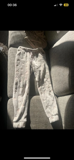 Mjukisbyxor med hjärtan och snörning - Supergosiga ljusbeige mjukisbyxor med rosa hjärtan på och bred satinliknande snörning i midjan. Byxorna har normal passform och är tillverkade i mjukt fleece-material, perfekta för att ha hemma. Resår vid benslutet. 