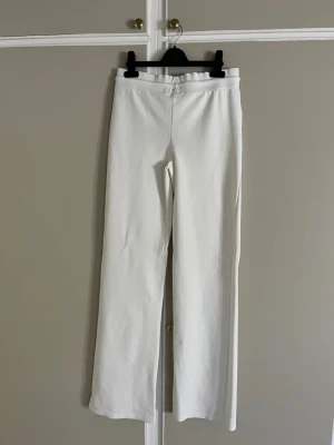 Vita wide mjukisbyxor med snörning - Snygga vita mjukisbyxor med breda ben och hög midja. Byxorna har en enkel design med snörning i midjan för extra komfort. Perfekta för en chill och avslappnad stil, tillverkade i mjukt material som känns skönt mot huden.