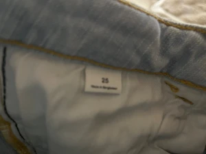 Ljusblå bootcut jeans storlek 25 - Snygga ljusblå jeans med bootcut passform och klassiska fickor med lock och knapp bak. Jeansen har normal midja och är tillverkade i mjukt denimtyg med gul kontrastsöm. Perfekta för dig som gillar retrovibbar och vill sticka ut.