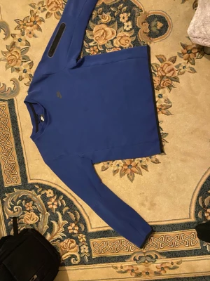 Blå långärmad Nike tröja S - Säljer en blå långärmad tröja från Nike i storlek S. Tröjan har en stilren design med rund hals och ett diskret Nike-logga på bröstet. Materialet känns mjukt och är troligtvis polyester, perfekt för träning eller chill. Ärmarna har en svart detalj på ena sidan.